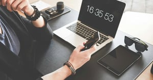 escritorio con una compuradora y las manos de una persona sosteniendo  un iphone
